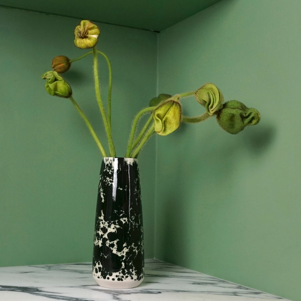 porcelain vase with black splatter glaze with poppy buds and a green background. 