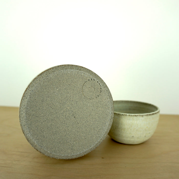 base detail of a handmade oil burner sitting on a birch ply table with a white background. showing the maker mark of Aku Ceramics. 