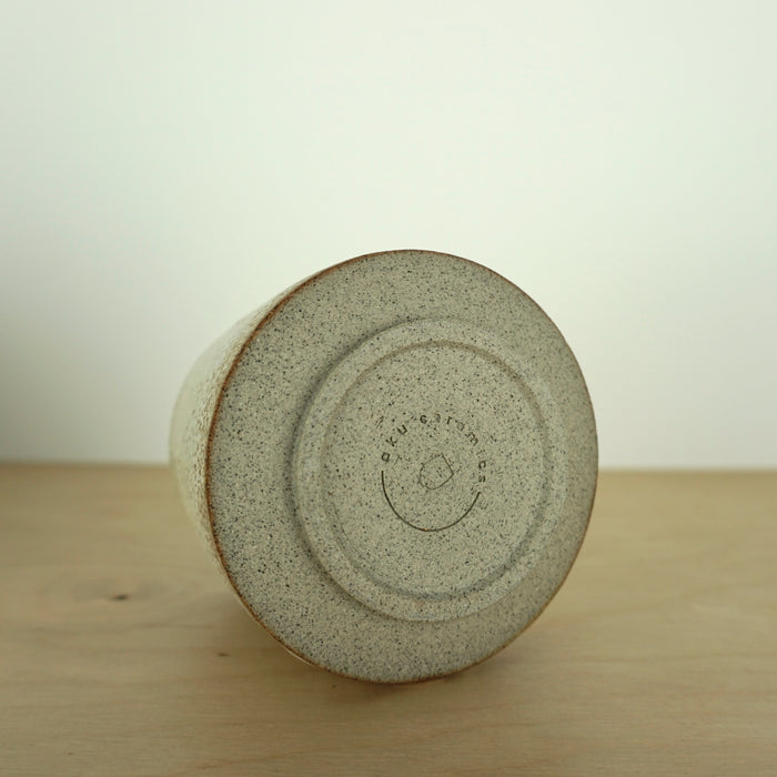 the base of an ivory Yunomi cup on a wooden table. Showing the makers mark of Aku Ceramics. 