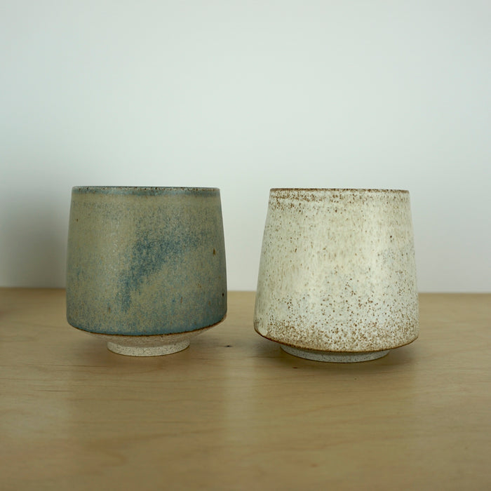 an ivory Yunomi cup and a blue grey Yunomi, side by side on a wooden table. 