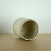 an ivory Yunomi cup on a wooden table. the cup is lying down so you can see inside. 