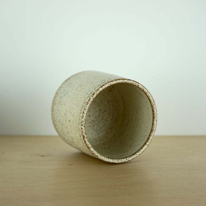 an ivory Yunomi cup on a wooden table. the cup is lying down so you can see inside. 