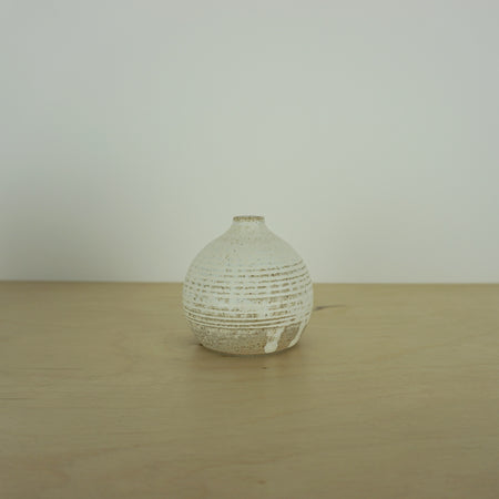 a small ivory coloured white handmade ceramic vase on a table. 