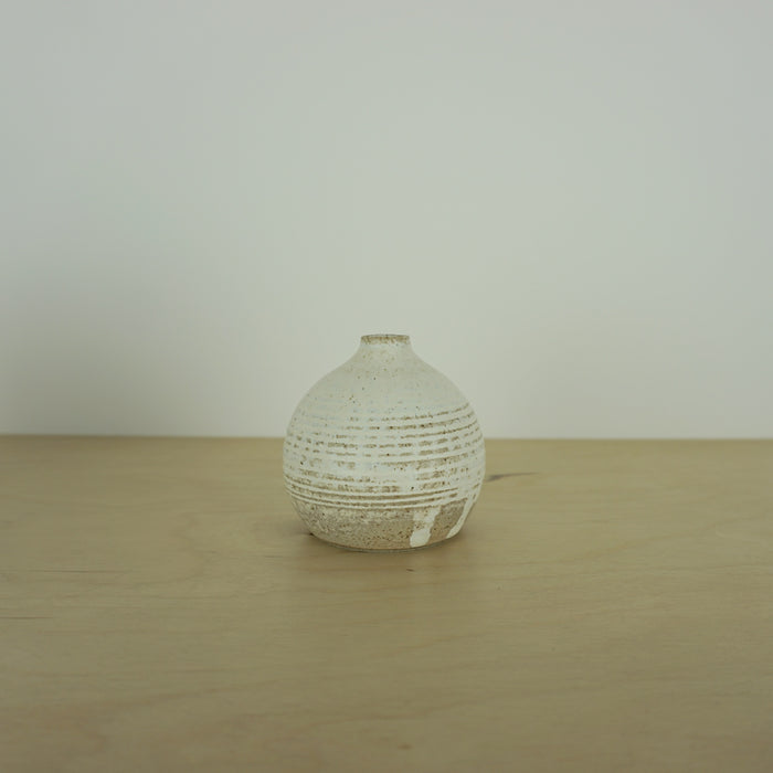 a small ivory coloured white handmade ceramic vase on a table. 