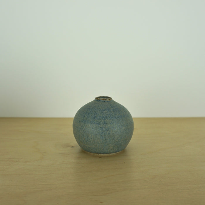 a small blue grey coloured handmade ceramic vase on a table. 