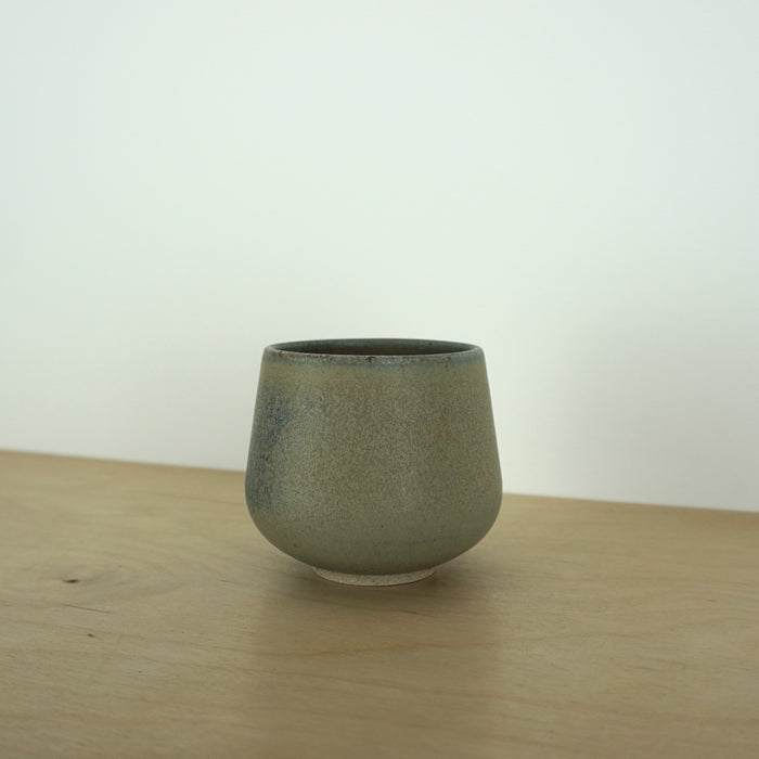 small handmade blue green cup on a wooden table and a white background. 