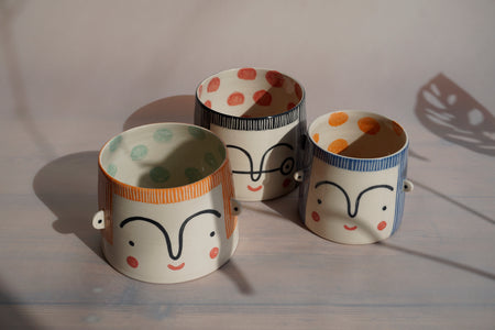 a group of three coloured planters. two large and one small. each with a face painted on. 