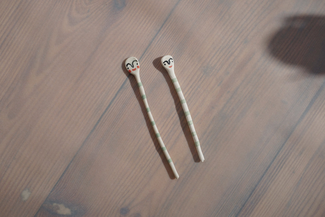 two green striped ceramic salt spoons by by Beci Callow with her signature faces painted on them. 