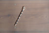 a ceramic salt spoon lying on a table in the sunshine. it has black stripes and a face painted on the end. 