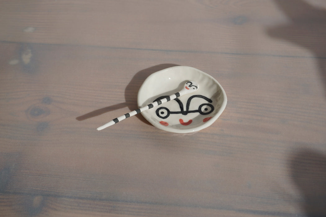 a salt dish and stripped salt spoon sitting on a table with faces painted on to them. 