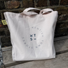 Costa Del Kentish Town Beach Bag on a wooden bench with the logo of Kentish Town stores. 