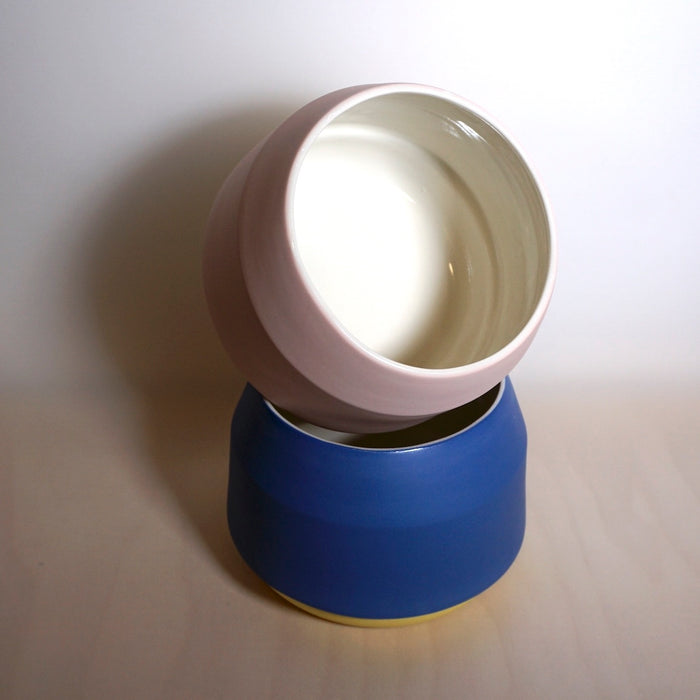 two ceramic planters stacked at an angle. one pink and white inside and the other blue with a yellow base. 