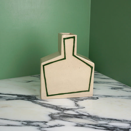 Angular vase with green outline on a marble table and a green background. 