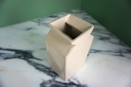 detail of the top of a cream coloured vase on a marble and green background.