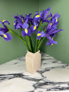 Cream coloured vase with a bunch of blue iris on a marble worktop with green background. 