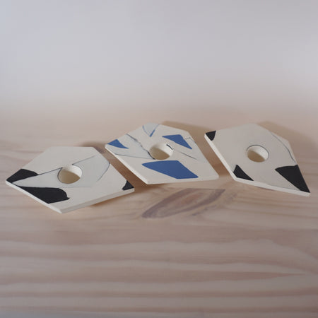 three abstract, angular candlestick holders in a line on a wooden table. 