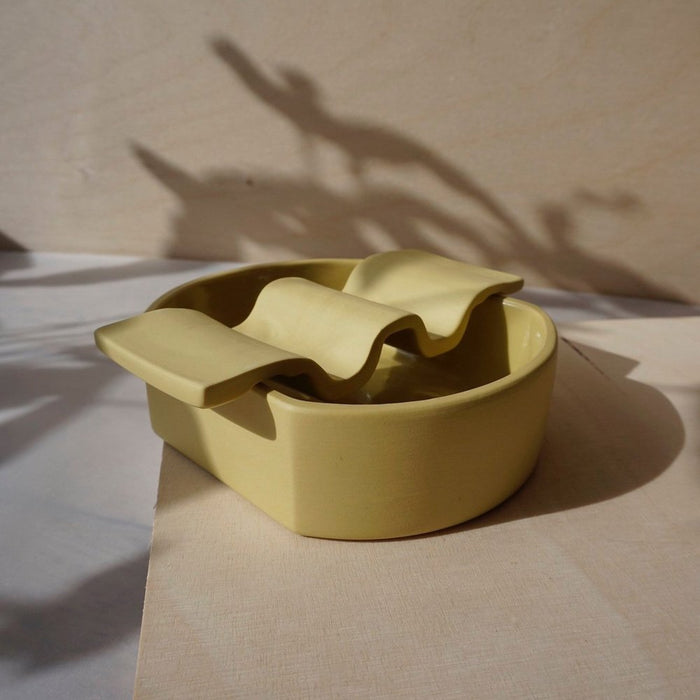 Yellow ceramic soap dish sitting on plywood. 