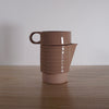 side view of a small handmade ceramic cup stacked into a ceramic jug. 