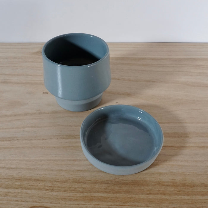 two parts of a planter and saucer for the planter sitting apart on a table. 