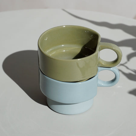 a stack of two hand poured slipcast ceramic cups - one green and one blue on a table. 