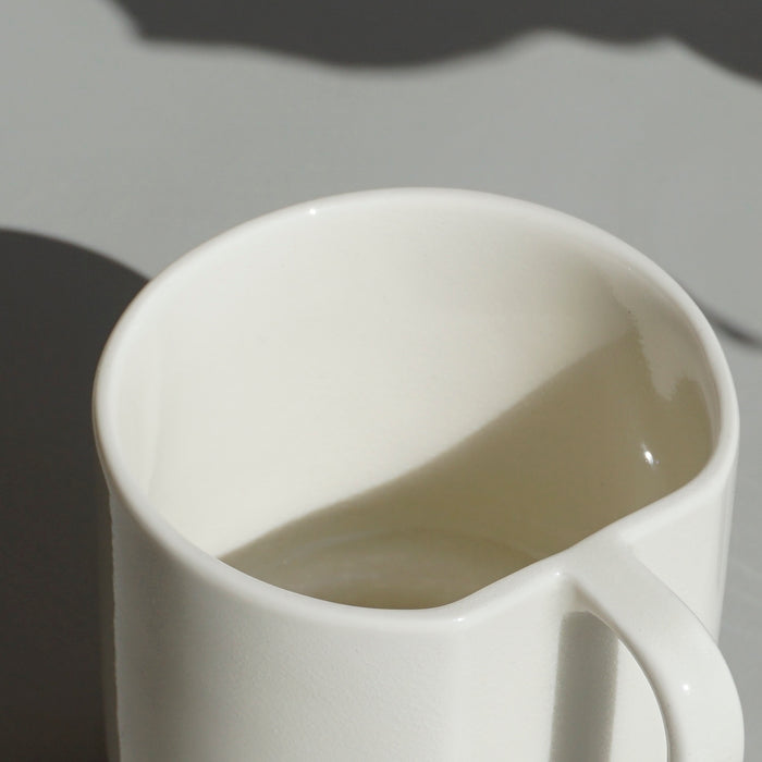 close up detail of a white slipcast mug with an angular handle by emma johnson ceramics. 