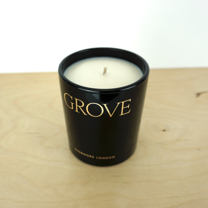 Evermore London candle glass jar on a wooden table. the jar is black with gold lettering that says grove. 