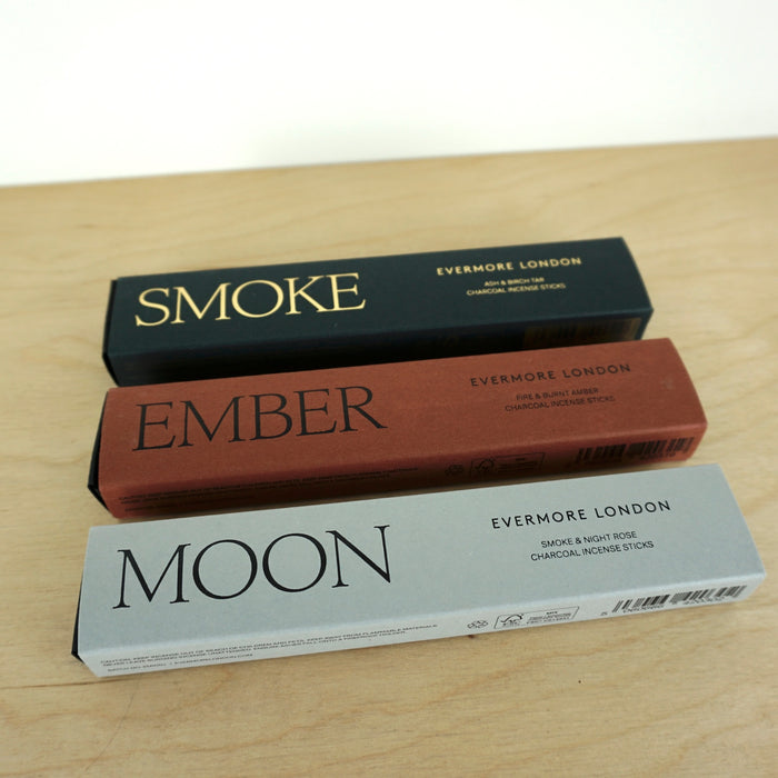 three boxes in grey, rust and black lying on a table. one called smoke, one called ember and one called moon. they are boxes of Incense sticks from Evermore london