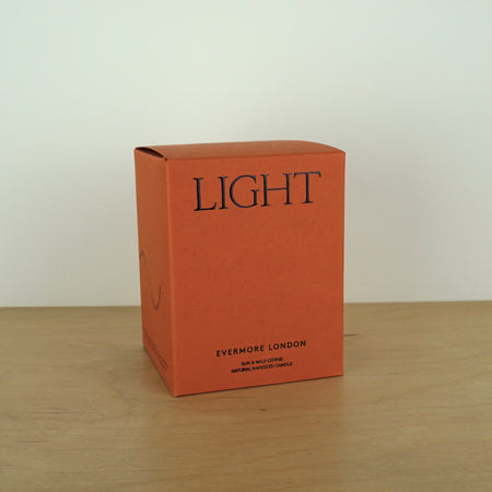 Evermore London candle box on a wooden table. the box is rust coloured with black lettering that says light. 