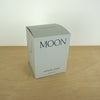 Evermore London candle box on a wooden table. the box is grey with black lettering that says moon. 