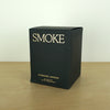 Evermore London candle box on a wooden table. the box is black with glod lettering that says smoke. 