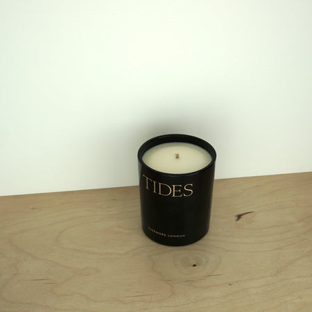 Evermore London candle glass jar on a wooden table. the jar is black with gold lettering that says tides. 