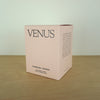 Evermore London candle box on a wooden table. the box is pink with black lettering that says venus. 