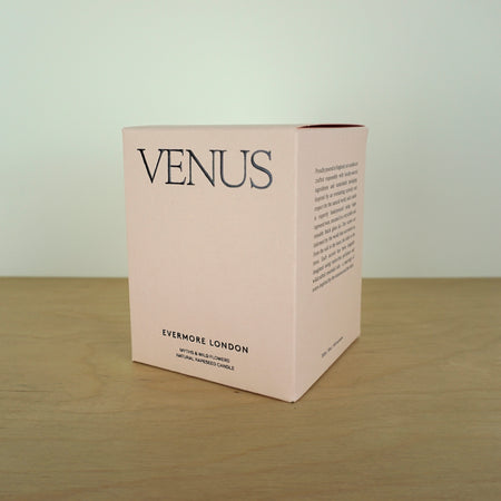 Evermore London candle box on a wooden table. the box is pink with black lettering that says venus. 