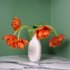 a white vase with drooping red tulips on a green background. 