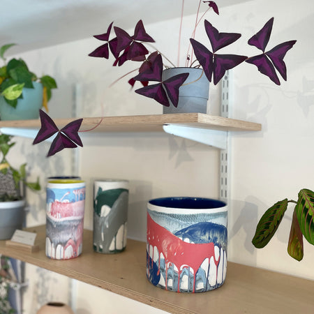 a large planter and three vases on a a shelf with some plants. 