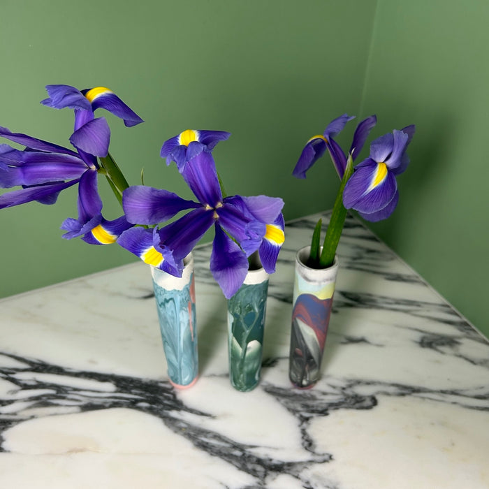 three bud vases, each with an iris in on a marble table with a green background. 