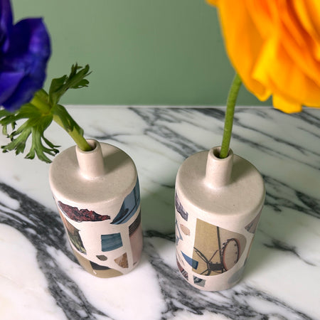 two bud vases with photo transfers on them on a marble table with a yellow and a blue flower just visible. 