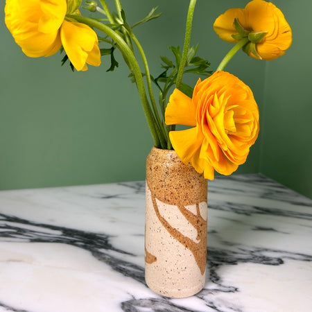 yellow flowers in a handmade ceramic vase with a drip brown glaze on a bright green background. 