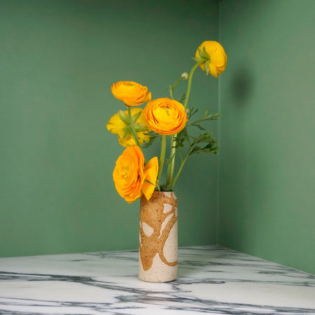 yellow flowers in a handmade ceramic vase with a drip brown glaze on a bright green background. 