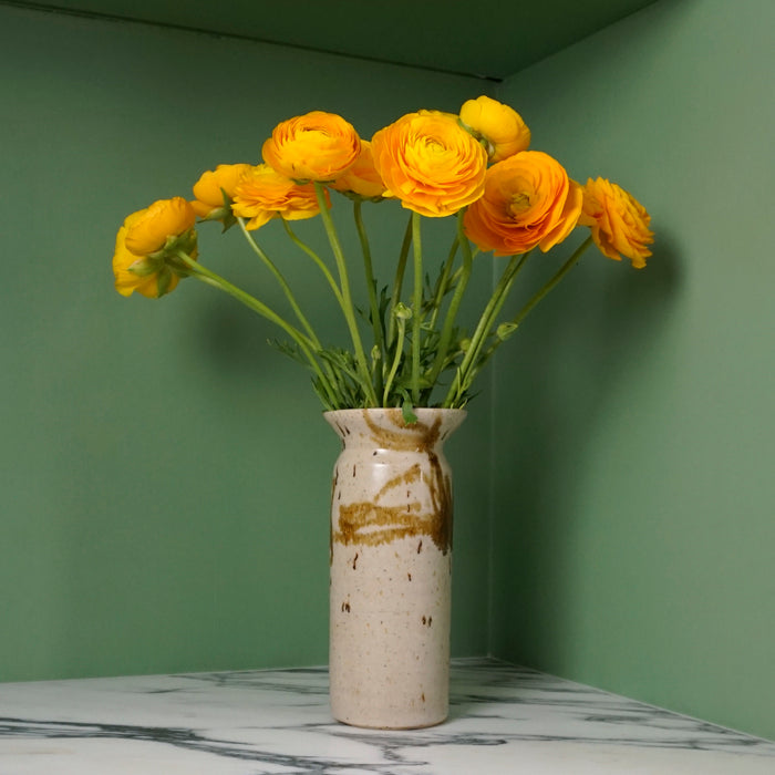 handmade ceramic vase on a marble table with yellow flowers on a bright green background. 