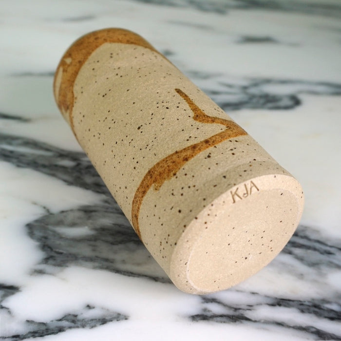 handmade ceramic vase with a drip brown glaze lying on a marble table so you can see the makers mark of KJA ceramics in the base. 