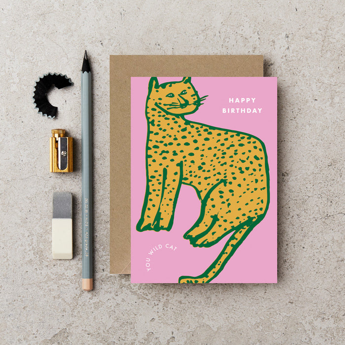 a pink card with a yellow cheetah on it and it says "happy birthday, you wild cat" 
