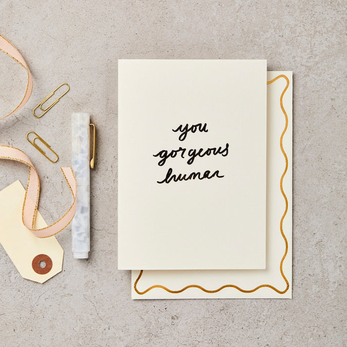 a white card with black italic text that reads "you gorgeous human". 