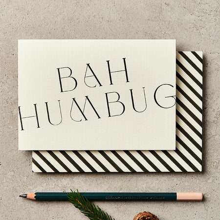 a hand printed Christmas card sitting on a table next to a pencil. the card reads Bah Humbug