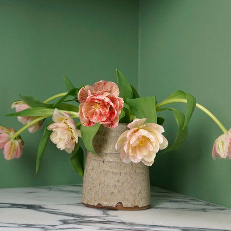 bunch of tuplis in a handmade vase on a marble table with green background. 