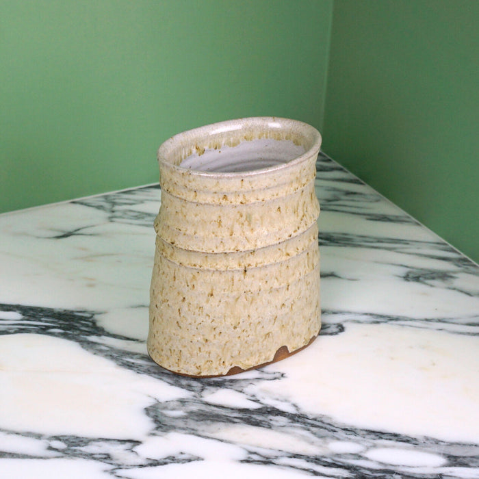 an oval vase in a willow ash glaze on a marble table. 