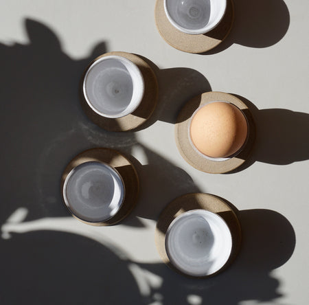 five egg cups photographed from above. one has an egg in it. the others show the white glaze. 