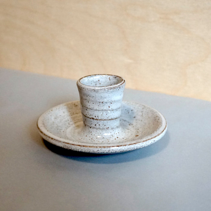 a candle stick holder on a light blue table with a tin white glaze. 