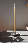 a tall beeswax candle in a candlestick holder in the bright sunshine. 