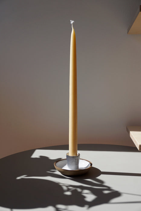 a tall beeswax candle in a candlestick holder in the bright sunshine. 